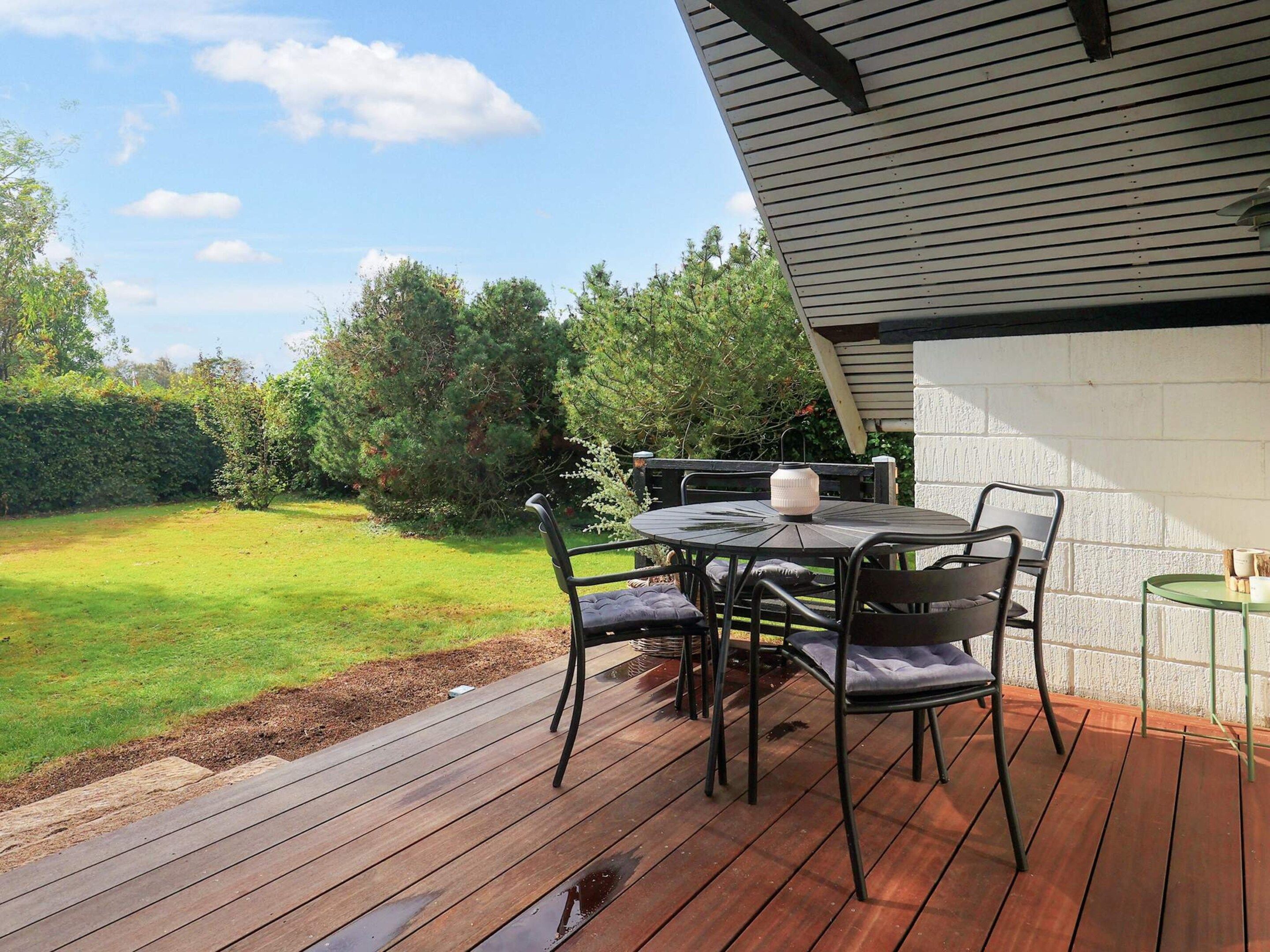 A deck with a table and chairs, overlooking a grassy yard with trees.