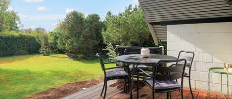 A deck with a table and chairs, overlooking a grassy yard with trees.