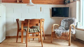 Une pièce chaleureuse avec une table et des chaises en bois, un fauteuil moelleux, un téléviseur fixé au mur et une fenêtre donnant sur un beau paysage.