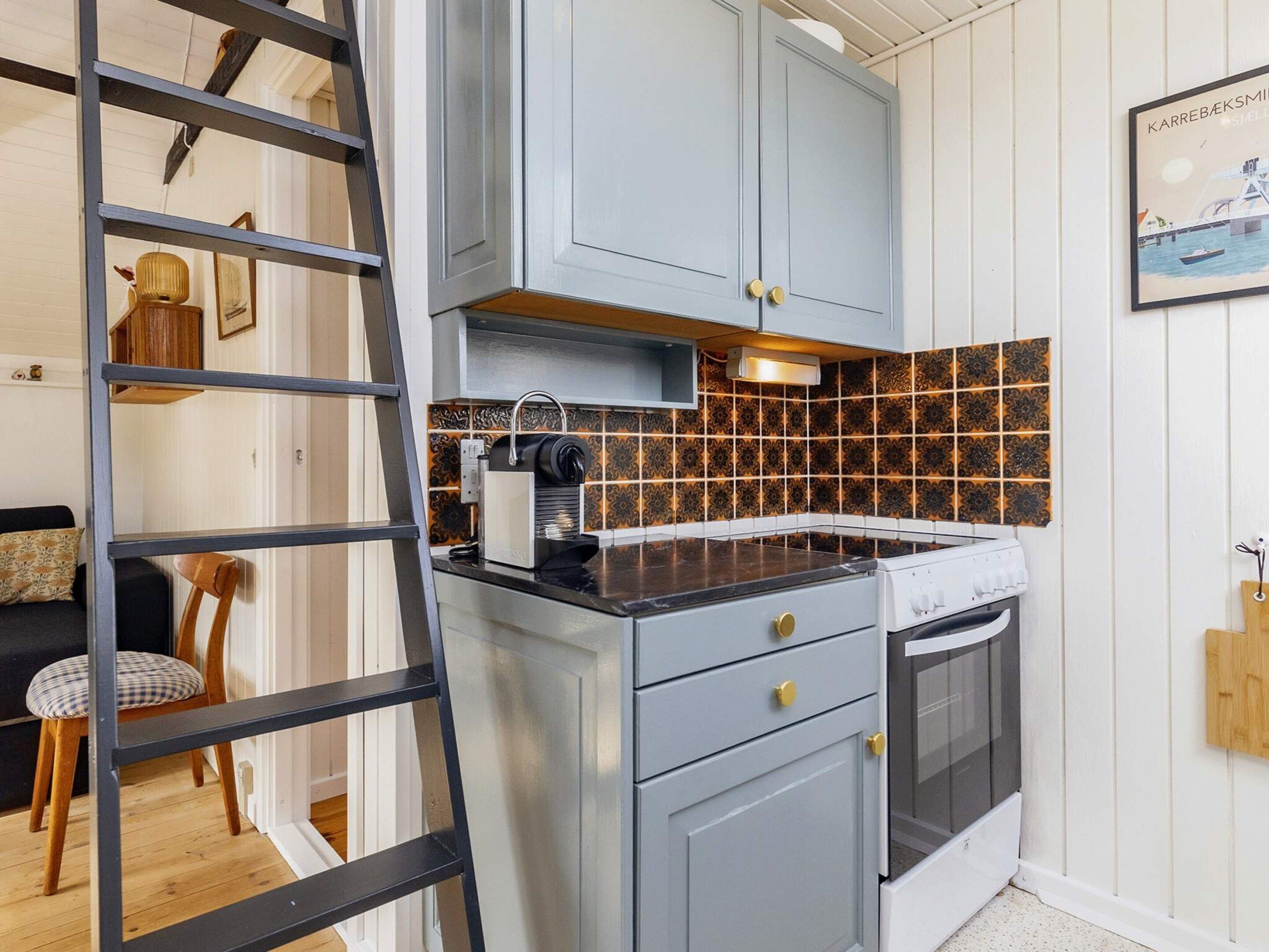 Een keuken met een inbouwfornuis, een koffiezetapparaat en een betegelde spatwand.