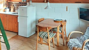 Une cuisine chaleureuse avec des meubles en bois, un réfrigérateur blanc, une table à manger avec des chaises et un téléviseur fixé au mur.