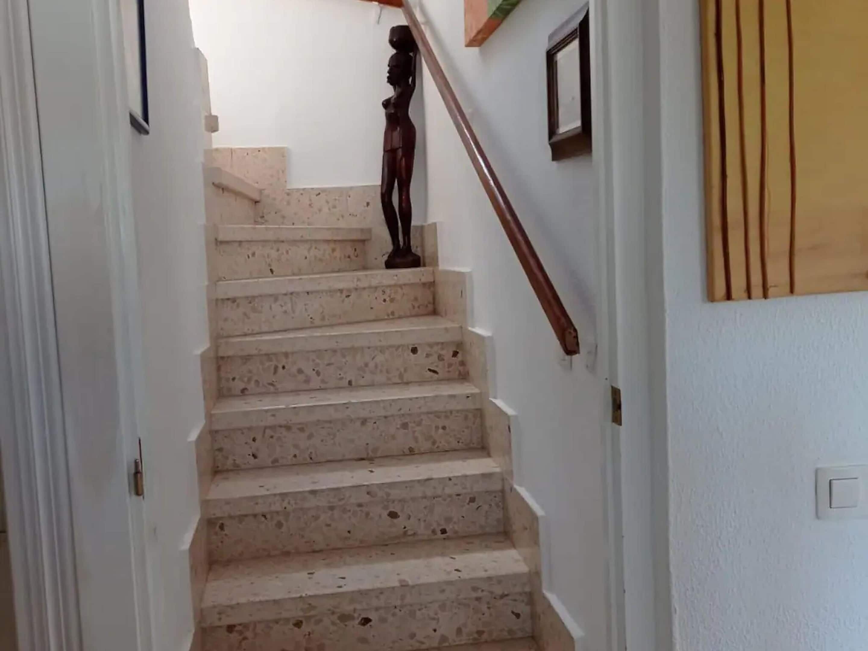 Una escalera con barandilla de madera y una pequeña estatua en la parte superior.