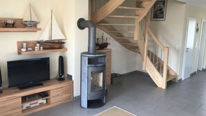 Una sala de estar con televisor, mueble de entretenimiento de madera, chimenea y una escalera de madera.