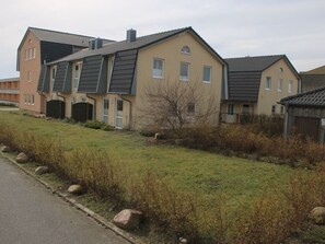 Eine Reihe moderner Wohngebäude mit flachem Dach, einer Grünfläche davor und einer befestigten Straße daneben.