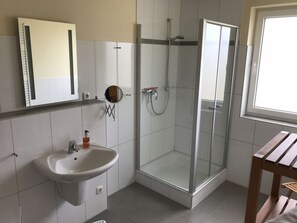 Ein Badezimmer mit Duschkabine aus Glas, einem Waschbecken mit Spiegel darüber und einer hölzernen Sitzbank.