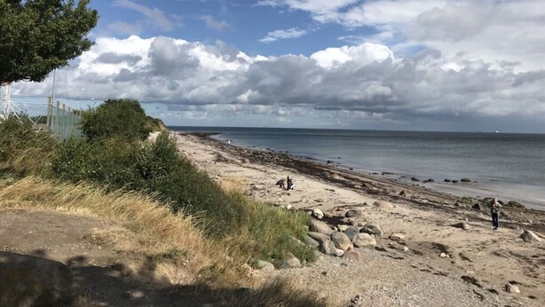 Una playa con cielo despejado, costa rocosa y algunas personas.