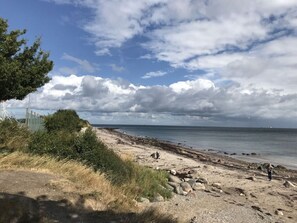 Ein Strand mit blauem Himmel, felsiger Küste und einigen Personen.