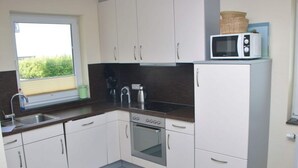 Una cocina compacta con armarios blancos, una estufa de acero inoxidable y un microondas sobre un mueble.