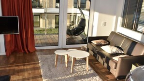 A modern living room with a sofa, two small tables, a TV, and a sliding glass door leading to a balcony. - "loft" Portmarina 26 (Bremerhaven)