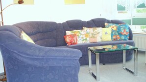 A living room with a blue sofa, a glass coffee table, and floral cushions. - Kurpark Residence Spot (Timmendorfer Strand)