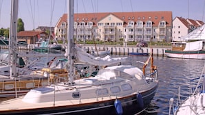 A marina with several sailboats docked, a row of multi-story buildings with balconies, and a clear sky. - Lake View Modern Retreat (Insel Poel)