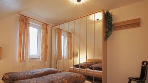 A bedroom with two beds, a chair, a window with curtains, a mirror, and a plant. - Lake View Modern Retreat (Insel Poel)