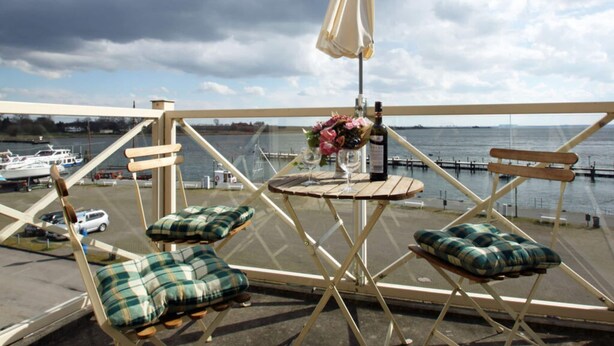 A balcony with two wooden chairs and a table, a white umbrella, and a view of the water and boats. - Lake View Modern Retreat (Insel Poel)