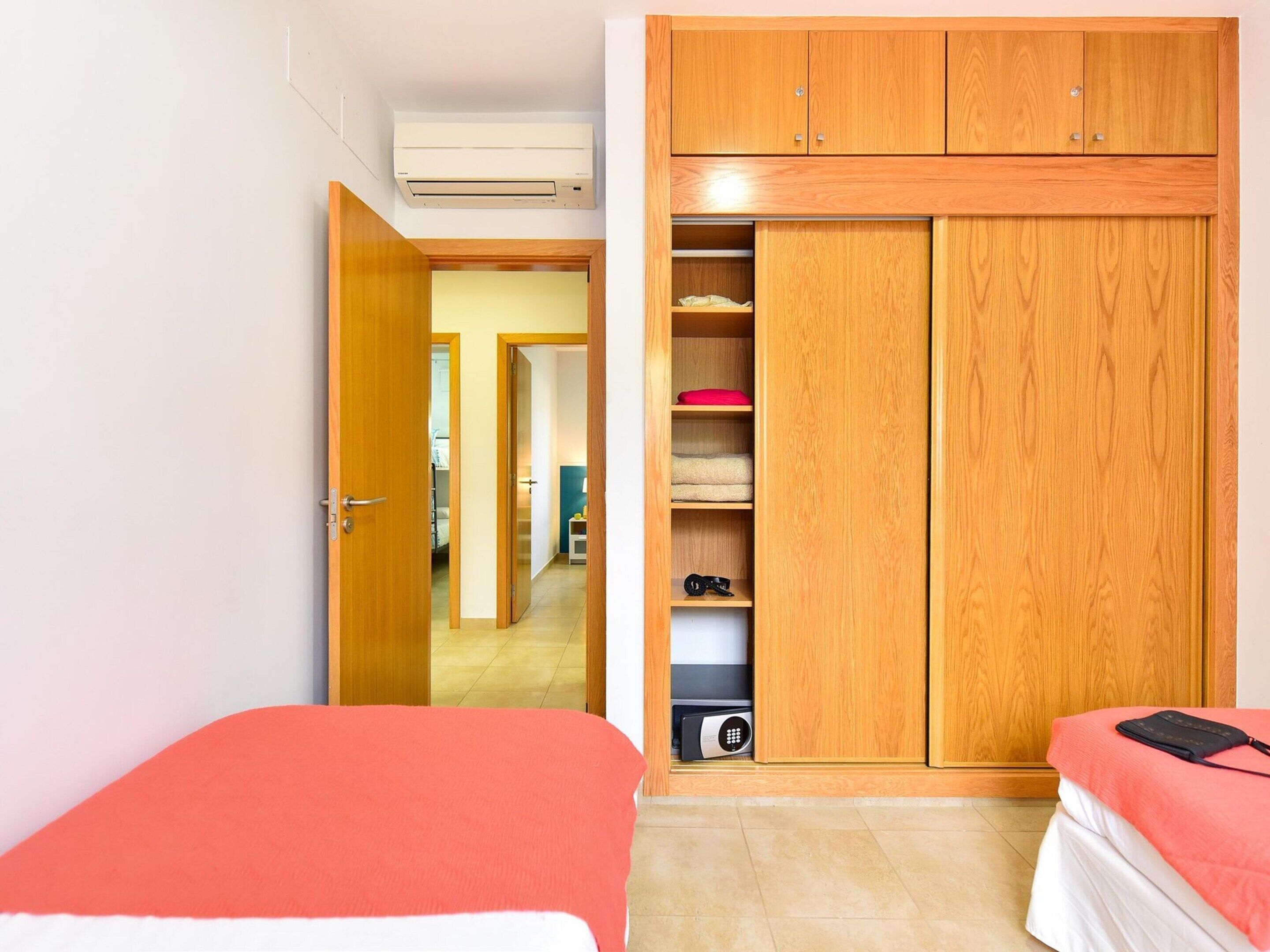 A bedroom with two beds, a wardrobe, and a hallway leading to another room.