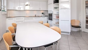 A modern kitchen with white cabinets, a large island with chairs, and built-in appliances. - 8 Person Holiday Home on a Holiday Park in Bogense (Bogense)