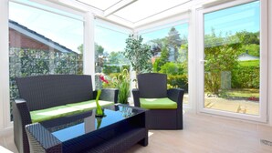 Ein sonnendurchflutetes Zimmer mit Glasdach, Korbmöbeln und Blick auf einen Garten.