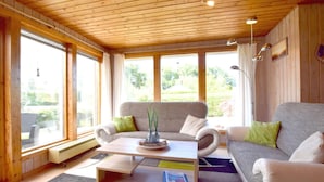 Ein gemütliches Wohnzimmer mit Holzboden, einem grauen Sofa, einem Couchtisch und Blick ins Grüne.