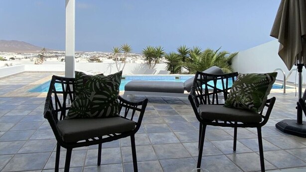 A terrace with two black chairs, a pool, and a view of a coastal landscape. - Mesmerising Apartment in Playa Blanca (Yaiza)