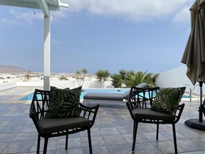Une terrasse avec deux chaises noires, une piscine et une vue sur un paysage côtier.