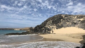 A beach with rocky cliffs, clear blue water, and a sandy shore. - Mesmerising Apartment in Playa Blanca (Yaiza)
