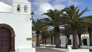 A white building with a bell tower, palm trees, and a clear sky. - Mesmerising Apartment in Playa Blanca (Yaiza)