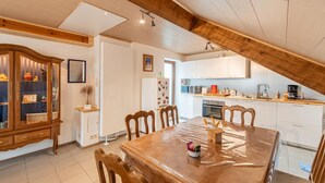 Un comedor con una mesa y sillas de madera, una cocina al fondo y un armario de madera con puertas de vidrio.