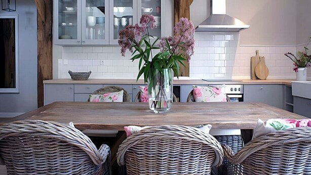 Una cucina moderna con un tavolo di legno, sedie in vimini e un vaso con fiori.
