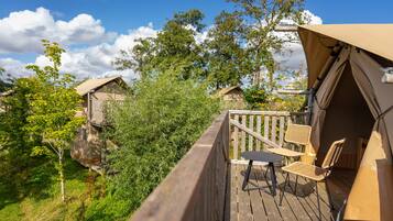A wooden deck with outdoor furniture, surrounded by greenery and a clear sky.