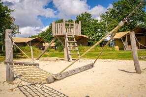 A wooden swing set with a rope net, a wooden climbing structure, and a sandy ground.