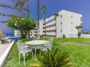 A white building with multiple balconies, surrounded by greenery and a pool. - Belvilla by OYO Apartment in Puerto de Santiago (Santiago del Teide)