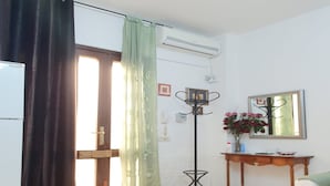 A living room with a sliding door, a standing fan, a mirror, and a small table with a vase of flowers. - Apartment in Matera Near Historic Center (Matera)