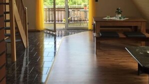 Una habitación amplia con una escalera de madera, un balcón con vistas a zonas verdes y una zona de comedor con mesa y sillas.