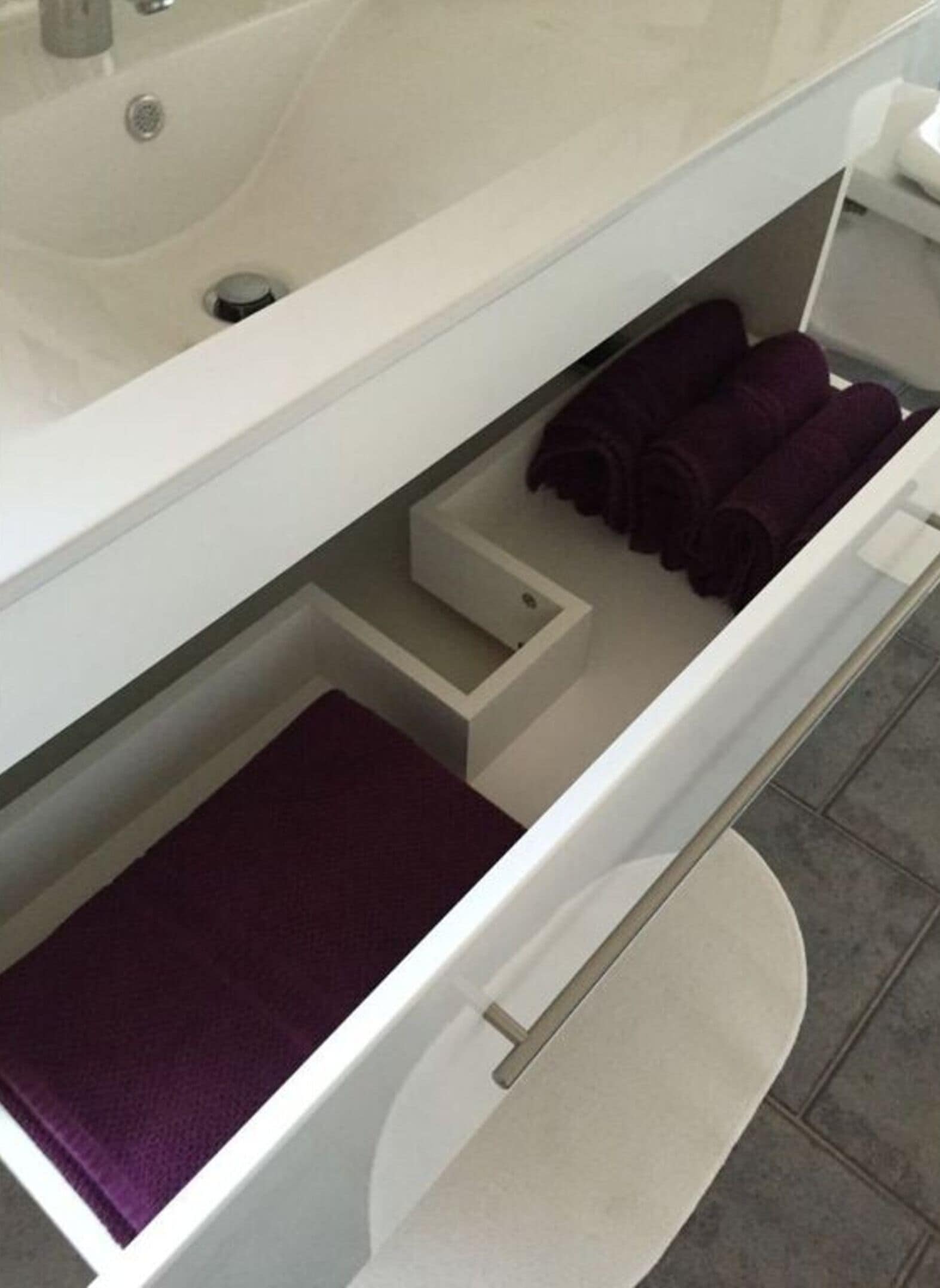 A bathroom with a white sink, a mirror, and a towel rack with rolled towels.