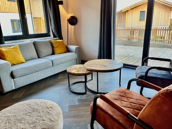 A modern living room with a grey sofa, two round wooden tables, and a single armchair.