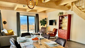 Un comedor con una mesa de madera preparada para cuatro personas, un armario rojo con cristalería y vistas a una terraza de madera a través de amplios ventanales.
