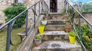 Edificio de piedra con una escalera que conduce a una puerta, rodeado de plantas en macetas y follaje.