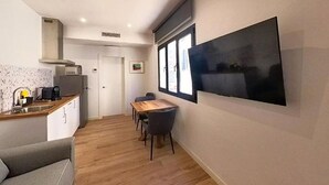 A compact kitchen with a dining area, a flat-screen TV mounted on the wall, and a window providing natural light. - Apartment in Puerto del Rosario Near Playa Chica (Puerto del Rosario)