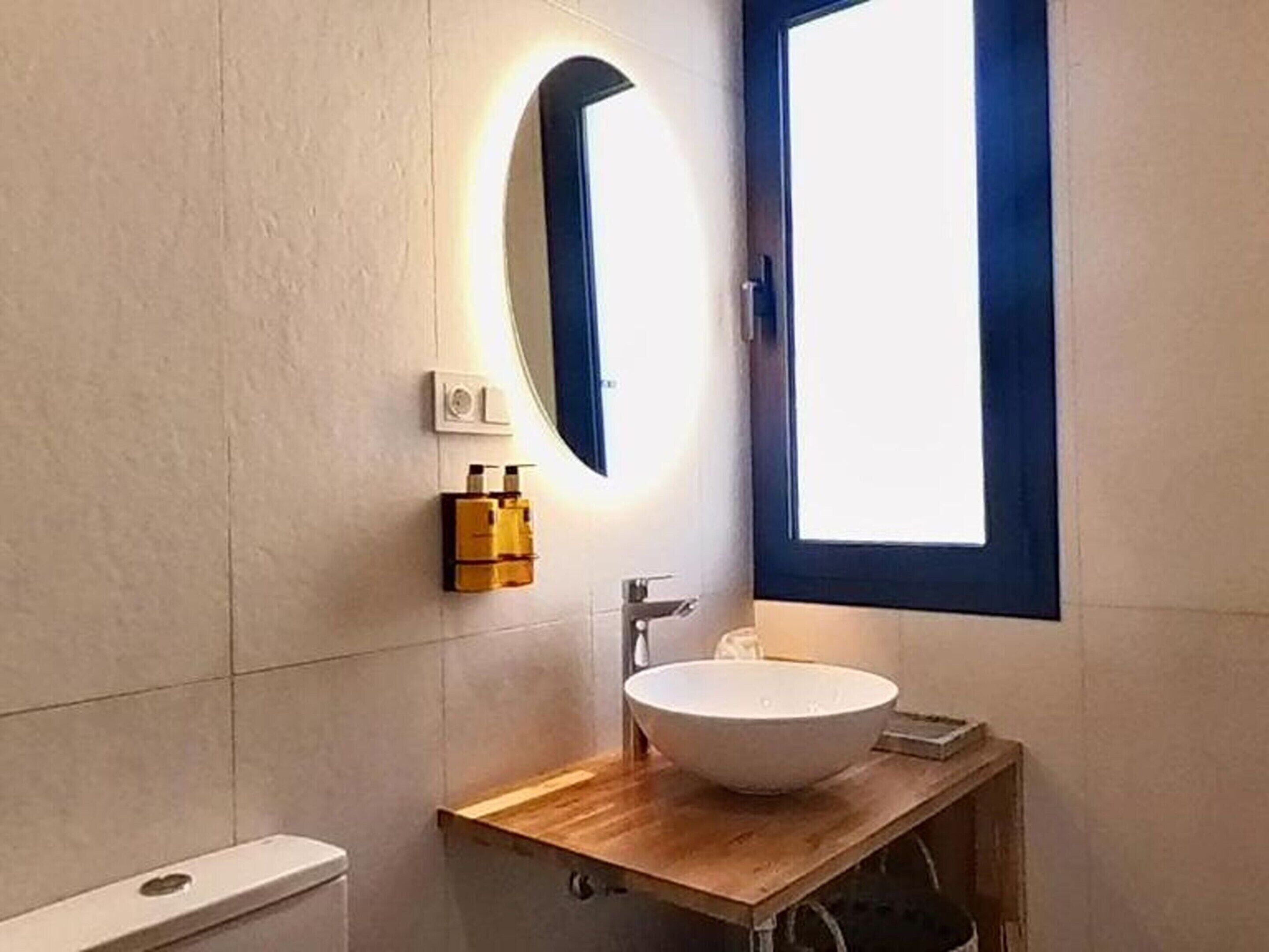 A bathroom with a round mirror, a white sink, and a window with a blue frame.