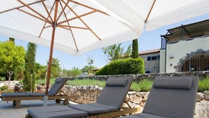 A sunlit outdoor seating area with wooden loungers and a large umbrella. - House of Olives Comfortable Holiday Residence (Dobrinj)