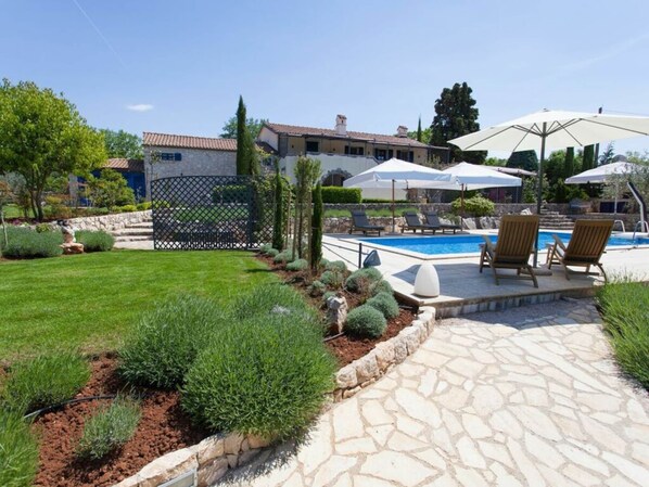 A pool area with lounge chairs and umbrellas, surrounded by a stone patio and a well-maintained lawn. - House of Olives Comfortable Holiday Residence (Dobrinj)