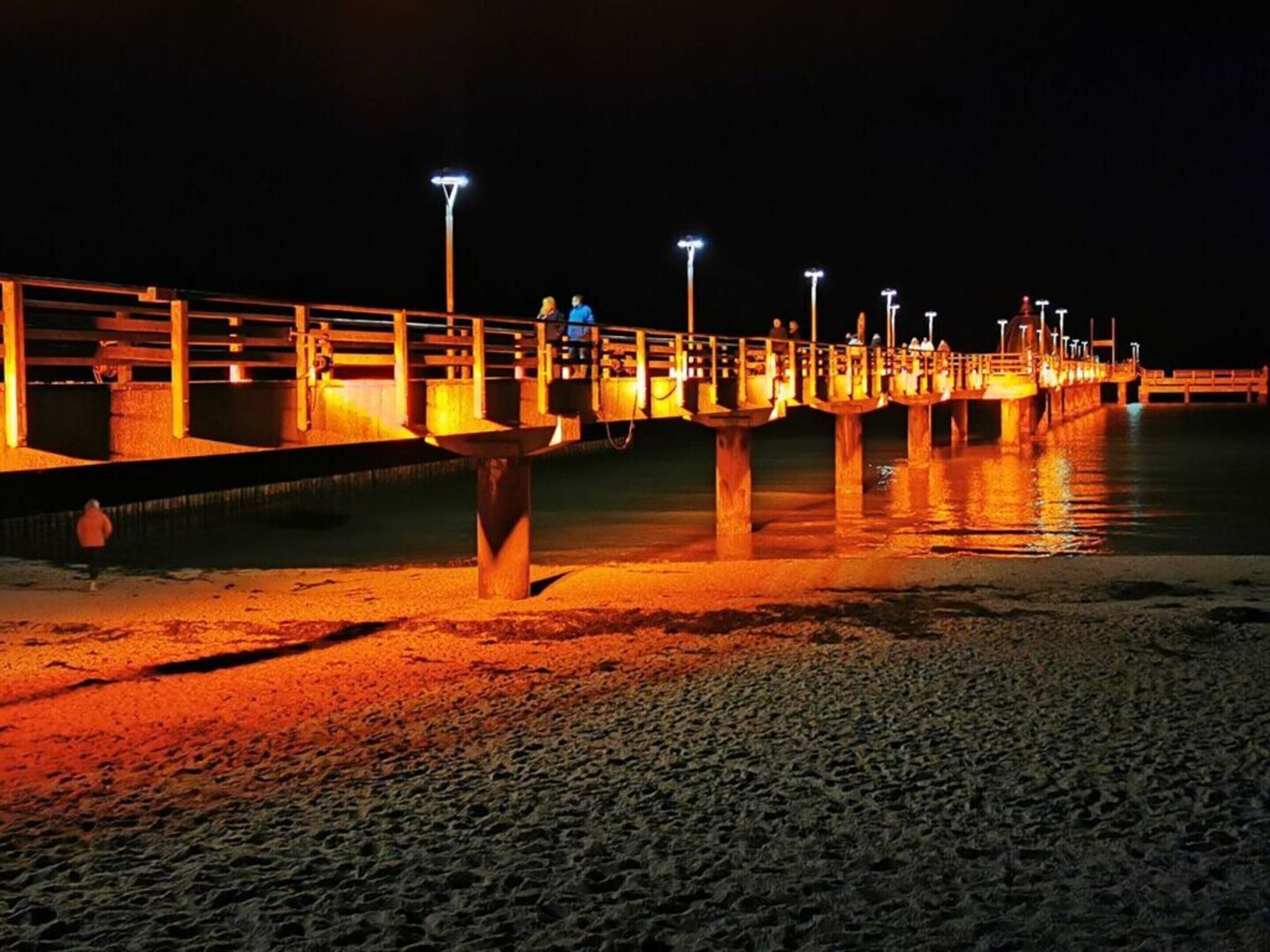 Een steiger die zich uitstrekt in het water, verlicht door lampen erboven.