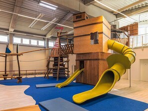 Un'area giochi al coperto con uno scivolo, strutture per arrampicata e un ponte sospeso.