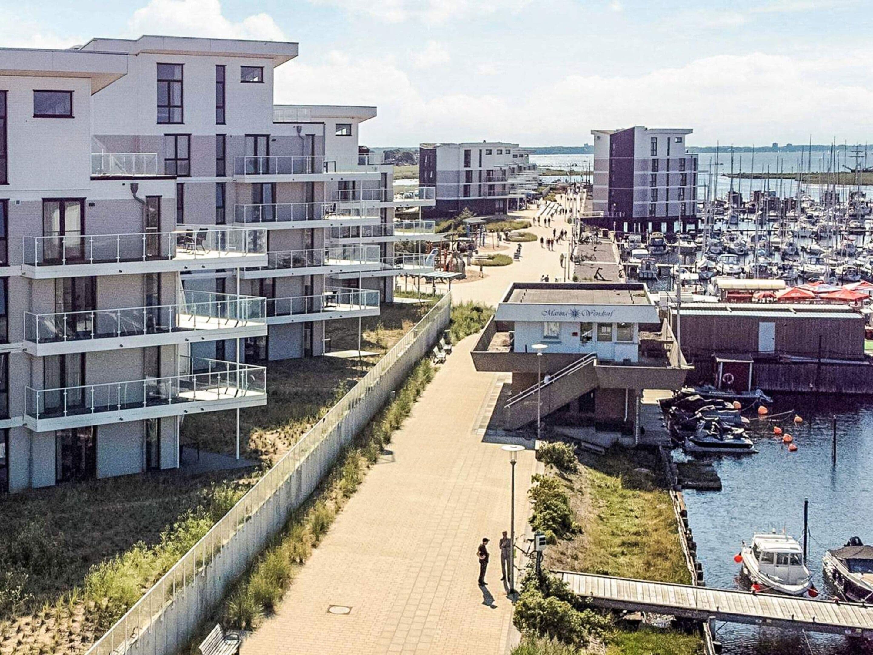Uma área residencial costeira com edifícios de apartamentos modernos, um porto com barcos e uma passarela para pedestres.