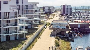 Uma área residencial costeira com edifícios de apartamentos modernos, um porto com barcos e uma passarela para pedestres.
