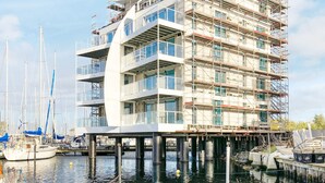 A multi-story building under construction with a waterfront view, featuring balconies and large windows. - Holiday Home in Wendtorf (Wendtorf)