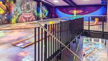 Un área temática del espacio con un mural de un astronauta y planetas, una escalera con barandillas metálicas y una zona de juegos con un tobogán.