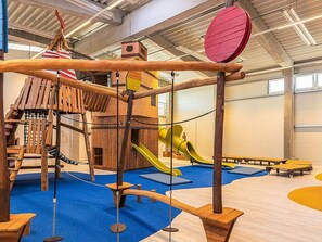 Un'area giochi con una struttura di arrampicata in legno, scivoli e un ponte sospeso.