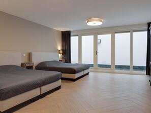 Habitación de hotel con dos camas, una mesita de noche, una lámpara y un amplio ventanal con vista al mar.