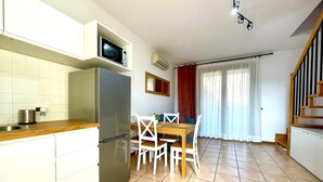 Uma cozinha compacta com micro-ondas embutido, geladeira e área de jantar com mesa de madeira e cadeiras brancas.