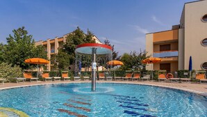 Piscina com espreguiçadeiras e guarda-sóis, cercada por edifícios.
